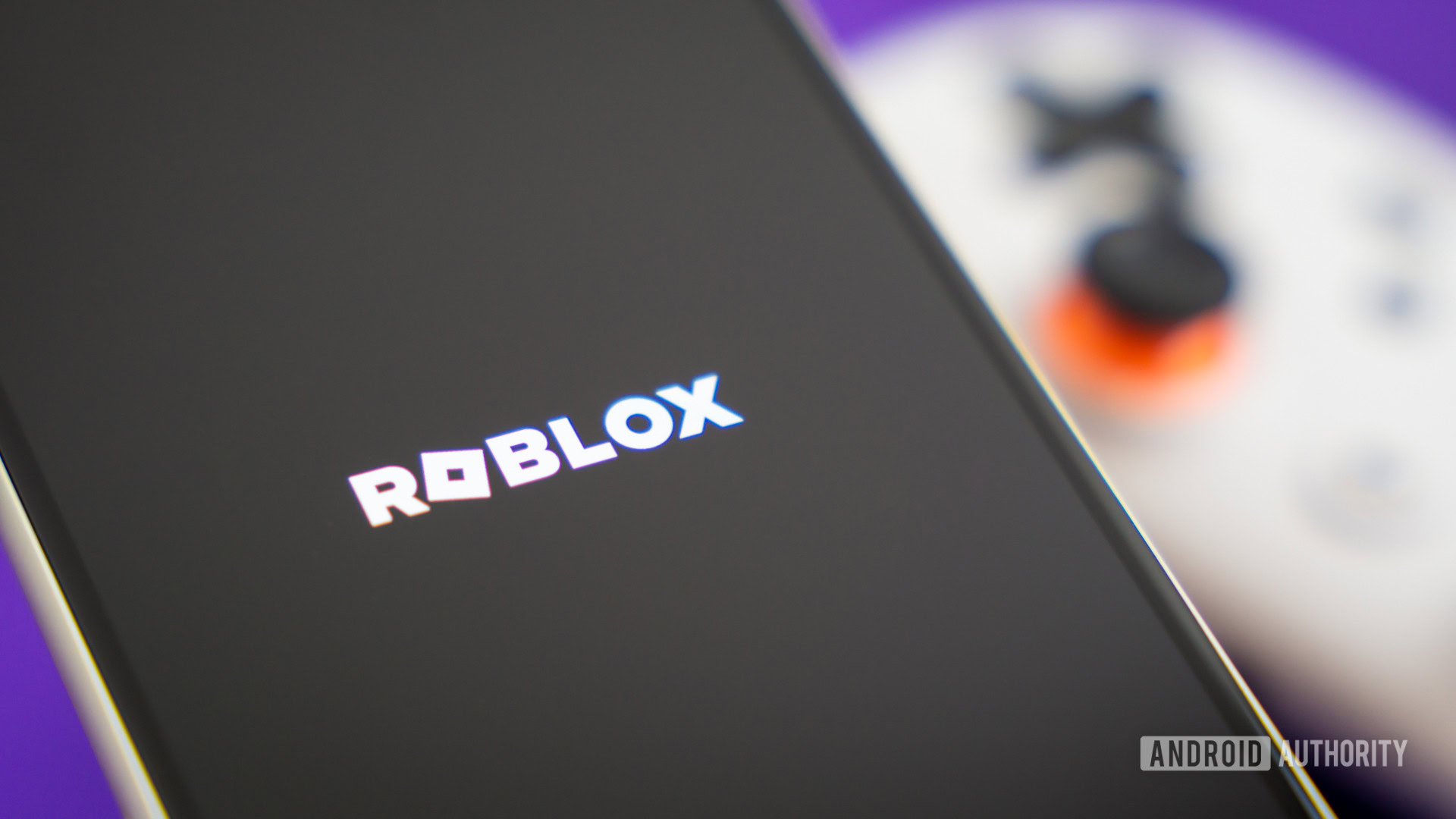 Roblox game logo on smartphone next to controller Stock photo 2