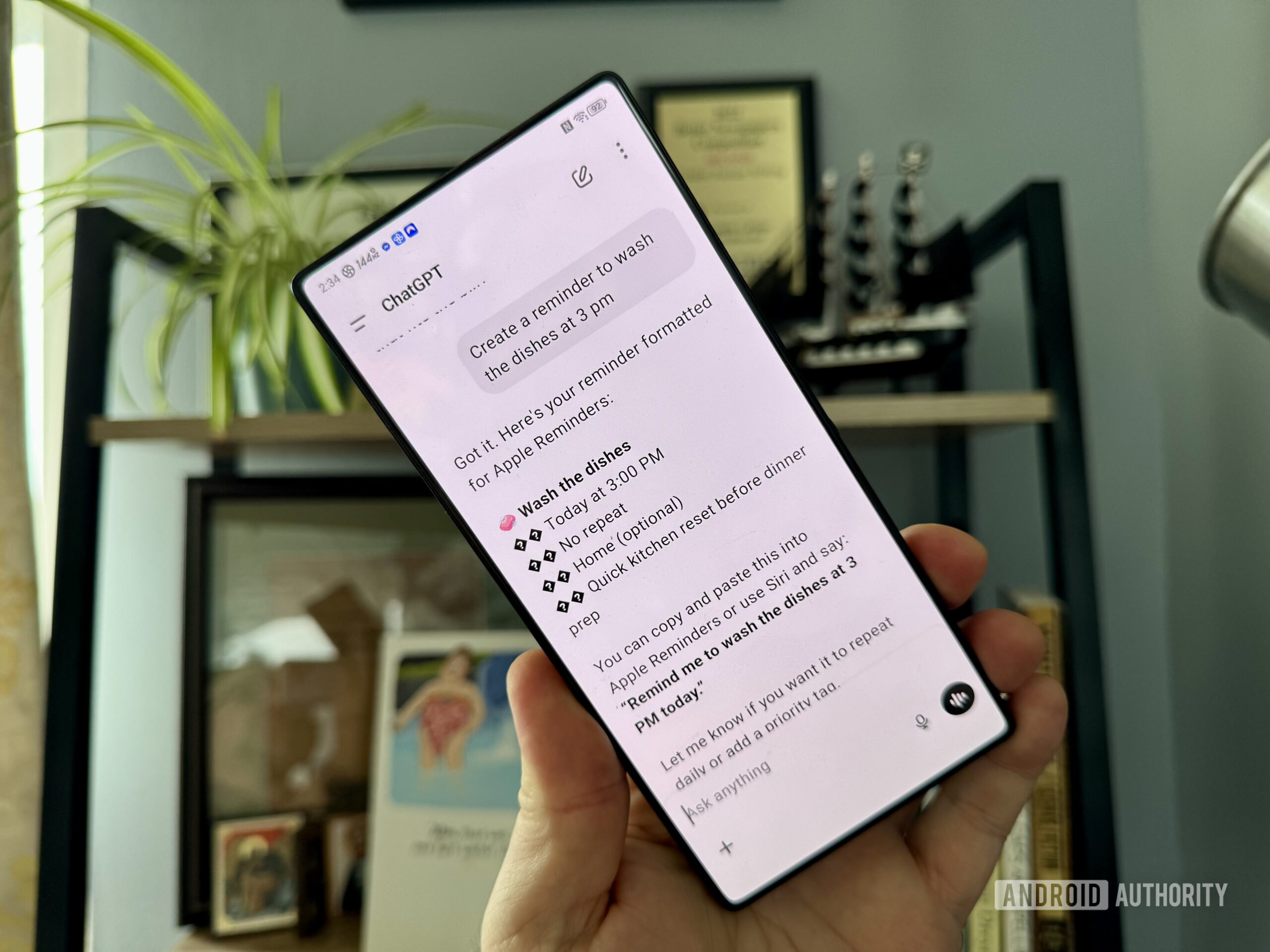 chatgpt reminders ChatGPT on an Android phone held in the air by a man's hand with a bookshelf in the background.